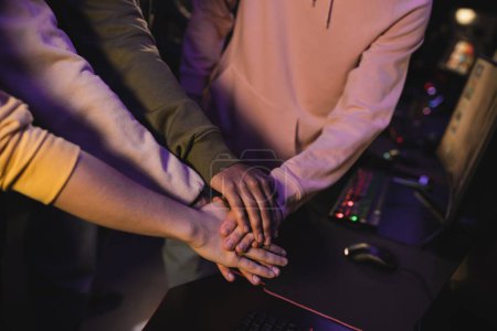 Cropped view of interracial friends holding hands in gaming club 