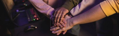 Cropped view of multiethnic gamers holding hands in cyber club, banner 
