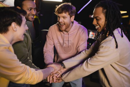 Photo for Cheerful multiethnic friends holding hands while spending time in gaming club - Royalty Free Image