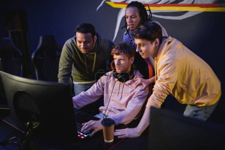 Multiethnic friends playing video game near coffee to go in gaming club 
