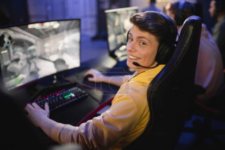 Smiling man in headphones looking at camera while playing video game in cyber club 