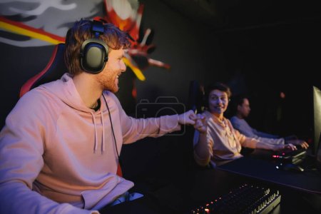 Photo for Cheerful gamer in headphones doing fist bump with blurred friend in gaming club - Royalty Free Image