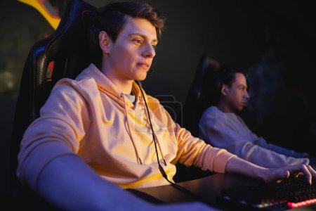 Young man using keyboard near blurred multiracial friend in gaming club 