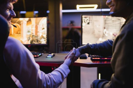 Foto de Jugadores positivos estrechando manos cerca de computadoras borrosas en el club de juego - Imagen libre de derechos