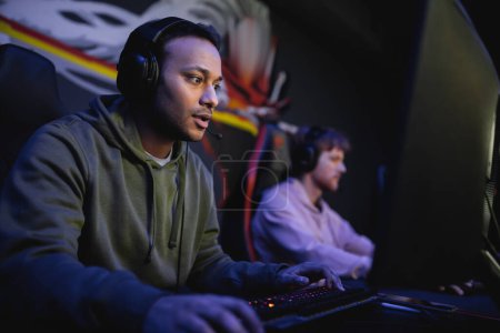 Photo for Indian player in headphones playing computer game with blurred friend in gaming club - Royalty Free Image