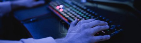 Cropped view of man using keyboard in cyber club with lighting, banner 
