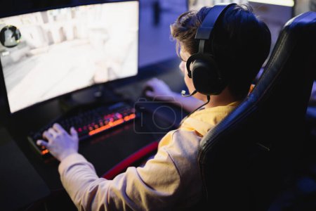 Téléchargez les photos : Jeune joueur dans un casque jouant à un jeu vidéo sur ordinateur dans un cyber-club - en image libre de droit