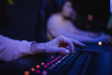 Cropped view of gamer using keyboard with lighting in cyber club 