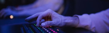 Cropped view of player using keyboard with lighting in cyber club, banner 