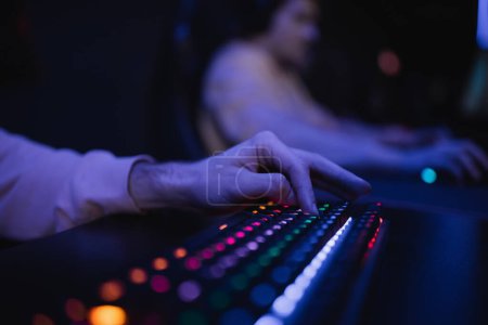 Cropped view of gamer using keyboard with colorful lighting in gaming club 