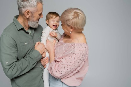 Älteres Paar umarmt glückliche Enkelin und lacht isoliert auf grau