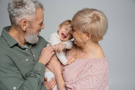 Téléchargez les photos : Excité tout-petit fille riant près heureux grands-parents isolés sur gris - en image libre de droit