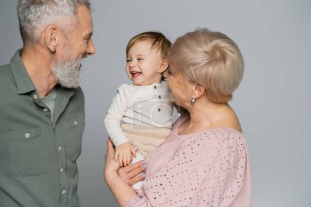 Téléchargez les photos : Grand-mère tenant heureuse petite-fille près de sourire mari barbu isolé sur gris - en image libre de droit