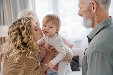 blonde curly woman kissing daughter during visit to mature parents