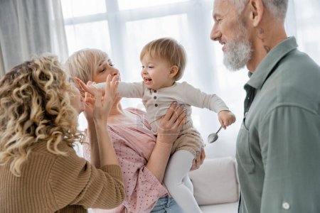 carefree baby touching face of mother near happy grandparents at home