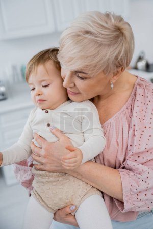 middle aged woman calming and embracing upset granddaughter in kitchen