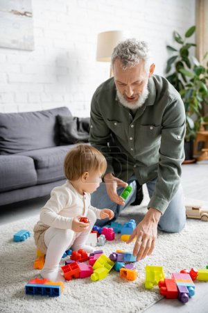 Bärtiger Mann und kleines Mädchen spielen mit bunten Bauklötzen auf Fußbodenteppich im Wohnzimmer