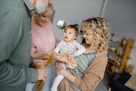 Téléchargez les photos : Fille étonnée regardant les grands-parents près heureuse mère bouclée dans le salon - en image libre de droit