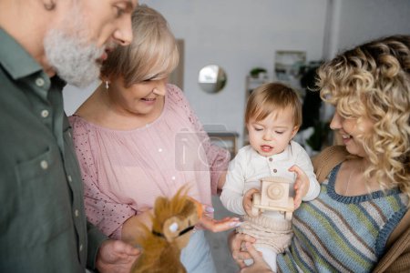 Kleines Kind sieht Spielzeugauto neben glücklichen Großeltern und Mutter im Wohnzimmer