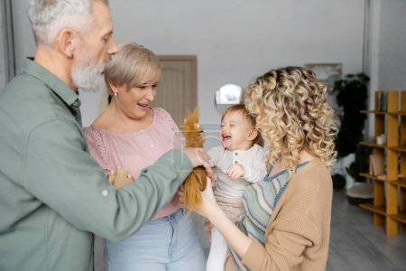 Bärtiger Mann hält Spielzeugpferd neben fröhlicher Enkelin und Familie im Wohnzimmer