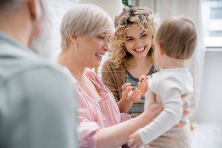 joyful women playing with toddler child at home in living room