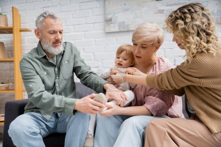 woman holding hand of little daughter near mature parents on sofa at home