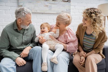 Sorgenfreies Kind lacht bei glücklichen Großeltern und Mutter auf dem heimischen Sofa