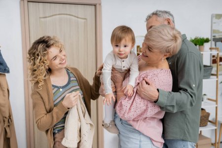 glückliche Frau mittleren Alters hält kleine Enkelin in der Nähe von Familie und Haustür