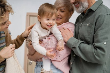 Kleines Kind lächelt bei glücklichen Großeltern und Mutter im Hausflur