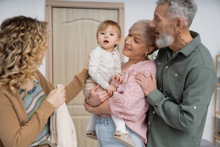Mädchen blickt in die Kamera bei glücklichen Großeltern und Mutter im Hausflur