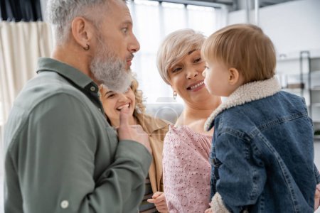 funny bearded man grimacing near little granddaughter and cheerful family at home