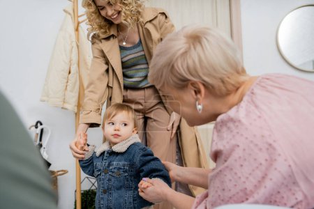 middle aged woman holding hand of granddaughter in denim jacket while meeting at home