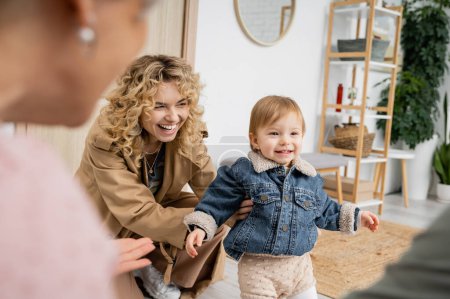 cheerful child in denim jacket smiling near happy mother and granny on blurred foreground 