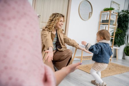 joyful woman in trench coat meeting daughter with outstretched hands near door at home