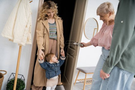 happy middle aged woman opening door to daughter with toddler girl at home