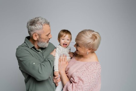 Foto de Niña emocionada riendo cerca de abuelos felices aislados en gris - Imagen libre de derechos