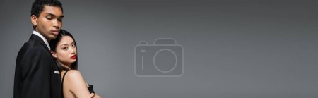 Téléchargez les photos : Élégante asiatique femme regardant caméra près élégant afro-américain homme isolé sur gris, bannière - en image libre de droit