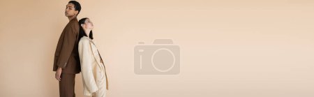 Photo for Young interracial couple in fashionable suit posing back to back isolated on beige, banner - Royalty Free Image