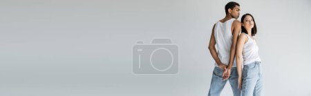 Téléchargez les photos : Jolie asiatique femme en jeans et débardeur posant près mince afro-américain gars isolé sur gris, bannière - en image libre de droit