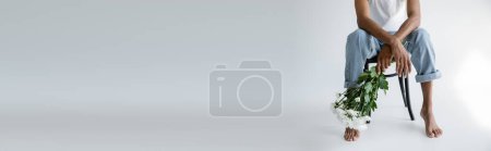 Photo for Partial view of barefoot african american man in jeans sitting on chair with bouquet on grey background, banner - Royalty Free Image