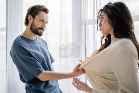Bearded man pulling clothes of girlfriend during conflict at home 