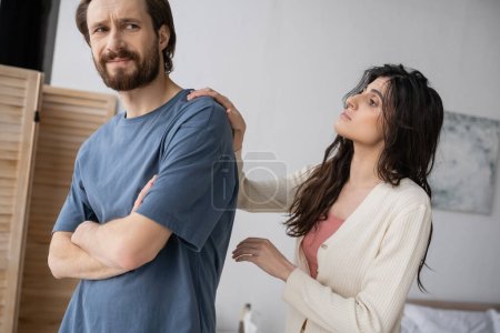Brunette woman calming down offended boyfriend with crossed arms at home 