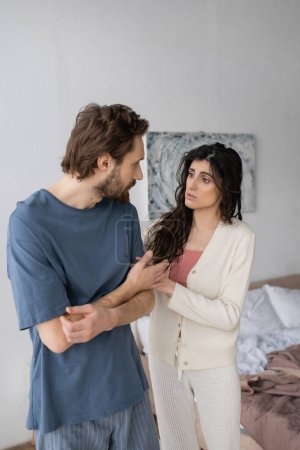 Morena mujer calmando molesto novio en pijama en el dormitorio 
