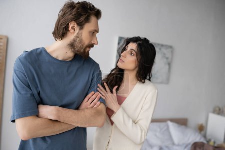 Brunette woman talking to displeased boyfriend during conflict in bedroom 