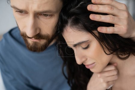 Bearded man calming and hugging displeased girlfriend at home 