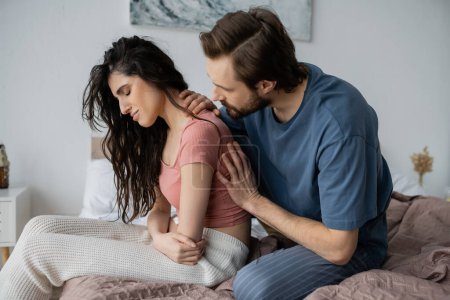Bearded man calming disappointed girlfriend in pajama in bedroom 