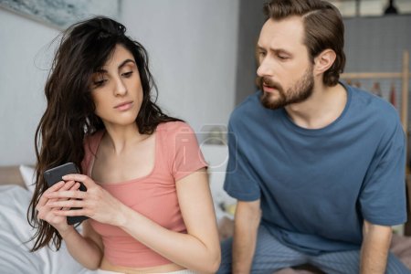 Téléchargez les photos : Brunette femme cachant téléphone portable près de petit ami jaloux dans la chambre - en image libre de droit