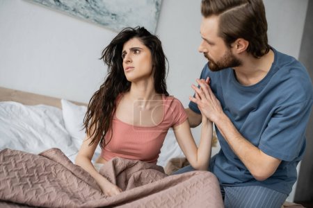 Brünette mann berühren hand von verärgert und asexuell freundin auf bett bei zuhause 
