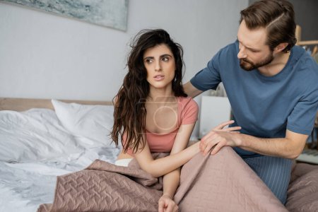 Asexual brunette woman sitting near bearded boyfriend on bed at home 