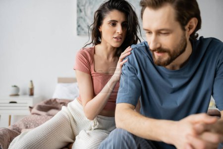Photo for Brunette woman in pajama calming down upset blurred boyfriend on bed - Royalty Free Image